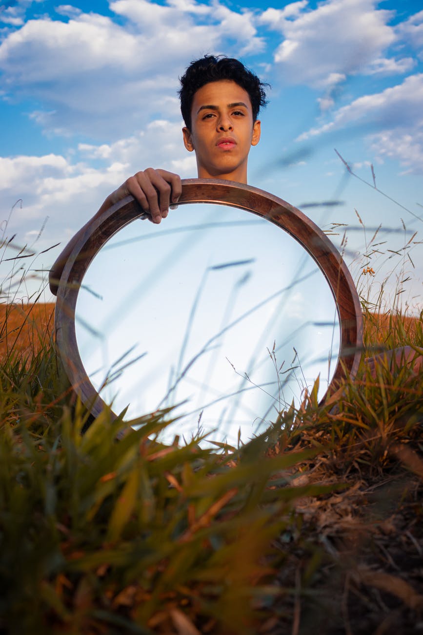 man holding a mirror standing on green grass field